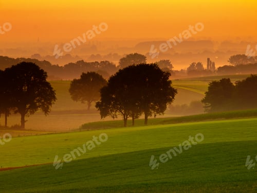 Preview: Orange sunrise over misty and hilly farmland
