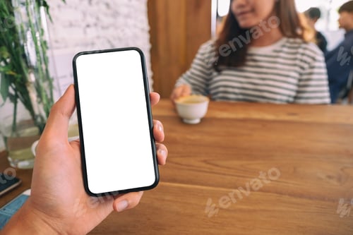 Preview: a man holding black mobile phone with blank white screen with woman sitting in cafe