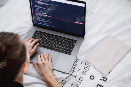 Preview: Young female programmer writes program code on a computer laptop in the bed at home. remote work