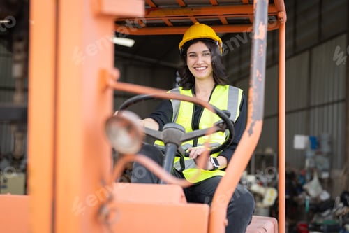 Preview: Smiling female worker driving forklift truck in factory