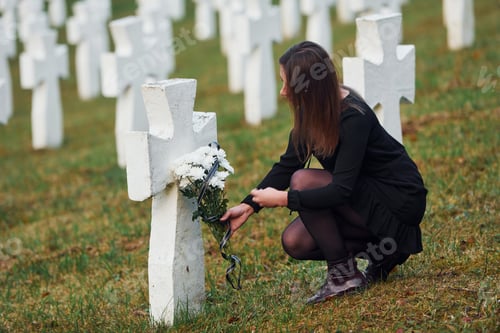Preview: Young woman in black clothes visiting cemetery with many white crosses