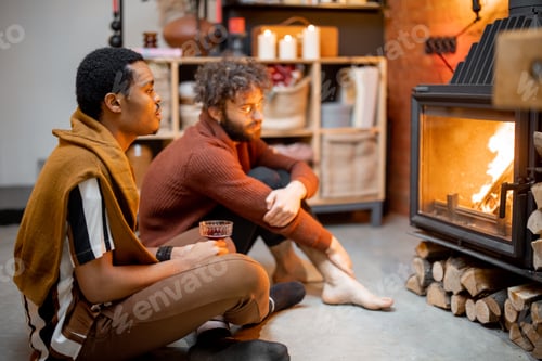 Preview: Two men sitting together by the burning fireplace at cozy home