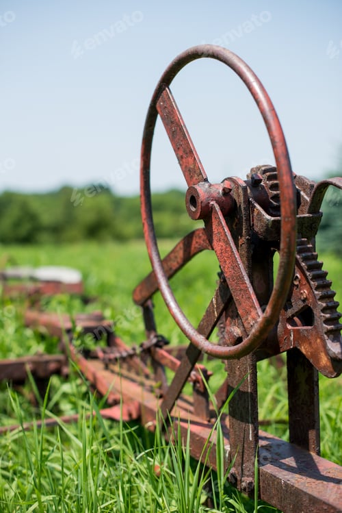 Preview: Vertical shot of an old rusted hay mower in a grass field.