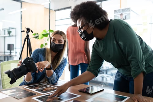 Vista previa: Diverso grupo de colegas de negocios con máscaras intercambian ideas mirando fotos en la sala de reuniones