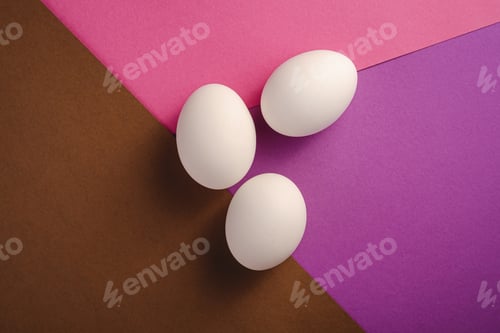 Preview: Three white eggs on purple, pink and brown colors plain minimal background