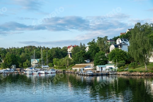 Preview: Archipelago, Stockholm Sweden. Seafront villa, yacht, reflection in ripple water, cloudy sky.