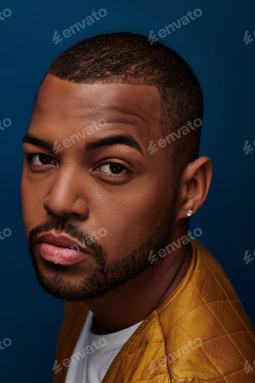 Preview: young bearded male model with diamond earring looking at camera with raised brow, fashion concept