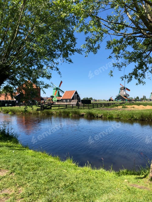 Preview: the small river with two windmills in the background and grass