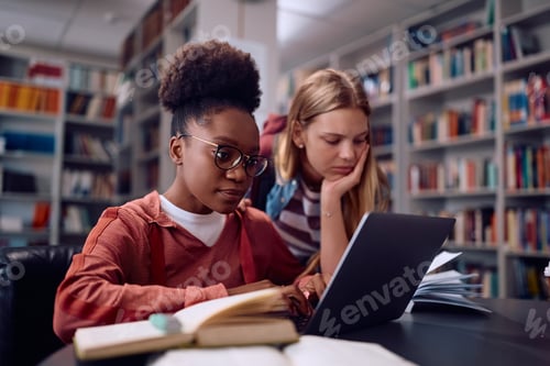 Preview: Black college student and her female friend using laptop while learning in library.