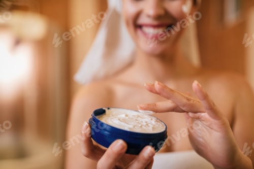 Preview: Cloe-up of woman using face cream in the bathroom.