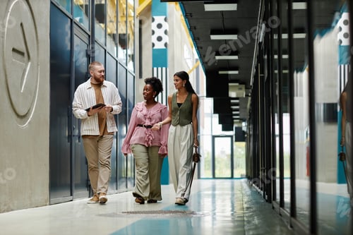 Preview: Team of Three Businesspeople Talking while Walking along Business Center Hallway