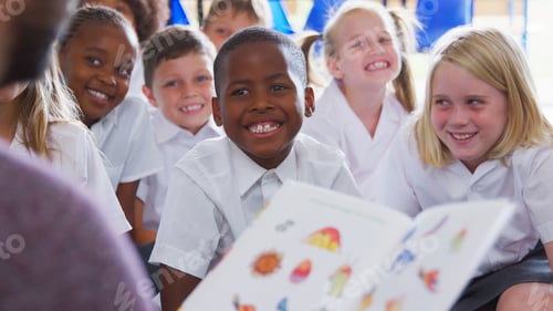 Preview: Male Teacher Reading Story To Group Of Elementary Pupils Wearing Uniform In School Classroom