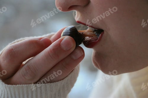 Preview: Minimalist image of woman taking a bite from a caramel covered in dark chocolate.