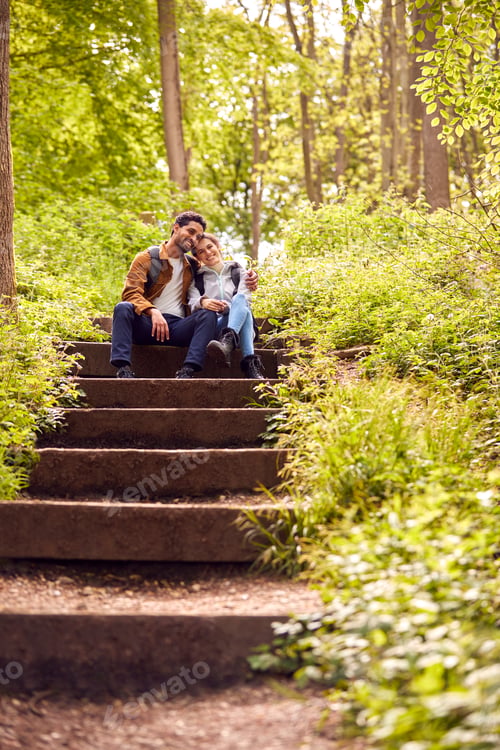 Preview: Hiking Couple With Backpacks Sitting On Steps On Path Through Trees In Countryside Together
