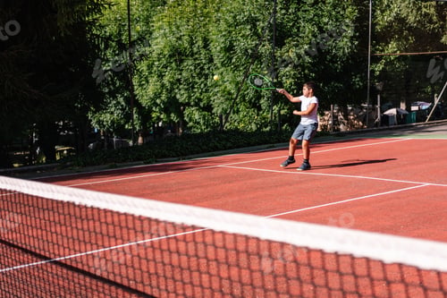 Preview: Young tennis player serving ball on clay court