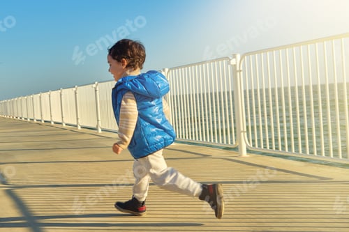 Preview: Happy little boy runs along the embankment. Active children's games. Happy childhood. Warm sunlight.