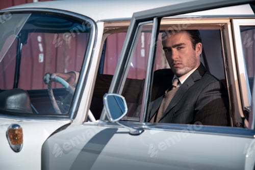 Preview: Retro 60S Fashion Business Man Wearing Grey Suit With Tie Sitting In Classic Car.
