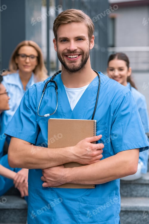 Preview: handsome caucasian medical student standing with notebook and looking at camera