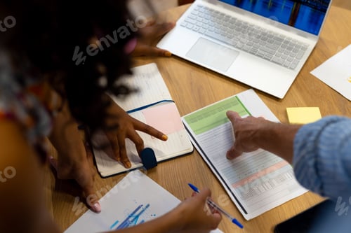 Preview: High angle view of diverse colleagues using laptop and documents in casual office meeting