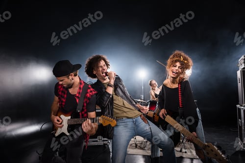 Preview: KYIV, UKRAINE - AUGUST 25, 2020: Curly vocalist singing in microphone while leaning on guitarist