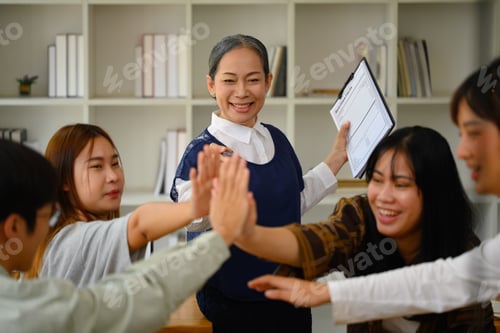 Preview: Cheerful mature professor with group of students celebrating project success in the classroom