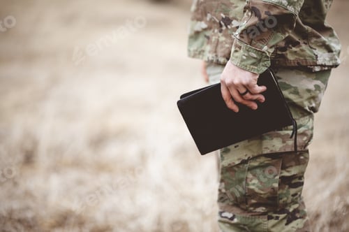 Preview: Shallow focus shot of a young soldier holding a bible in a field