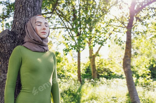 Preview: Young female in a hijab and casual clothes in the park. Protecting the environment