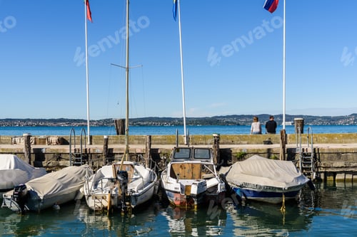 Preview: A wedding couple sitting with their backs on the harbor wall look at the lake on a weekend.
