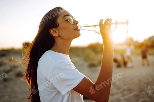 Preview: Pretty girl drinking beer at the beach at sunset. Young woman enjoying on beach holiday. Summertime