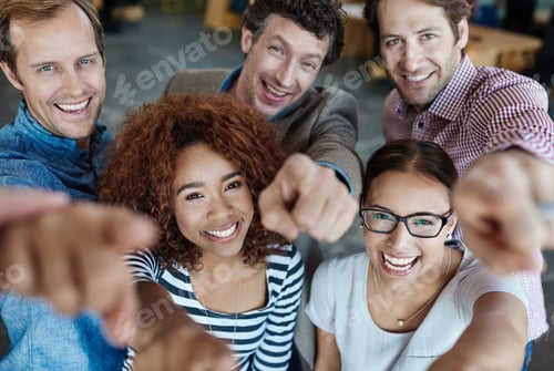 Preview: Portrait of a group of smiling coworkers pointing at the camera while standing in an office