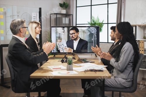 Preview: Group of multiethnical businesspeople clapping hands and looking at screen, having video conference