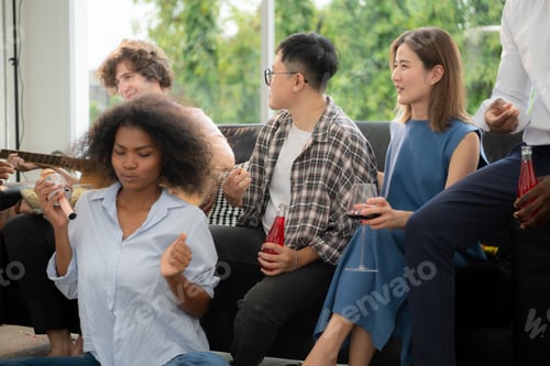 Preview: Group of multiethnic friends having fun at party by playing guitar and singing together at home.