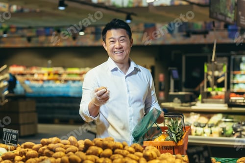 Preview: An Asian man is standing in a supermarket in the vegetable section, holding potatoes in his hands