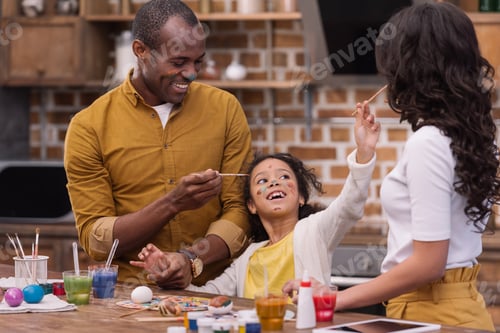 Preview: happy african american parents and daughter having fun while painting easter eggs