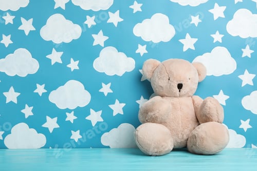 Preview: Teddy bear on wooden table near wall with painted blue sky, space for text. Baby room interior