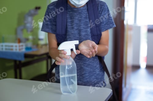 Preview: Caucasian schoolboy in classroom wearing choolbag disinfecting hands