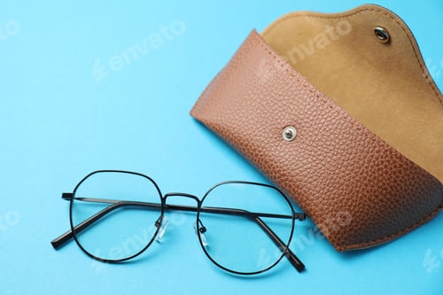 Preview: Case with stylish glasses on light blue background, flat lay