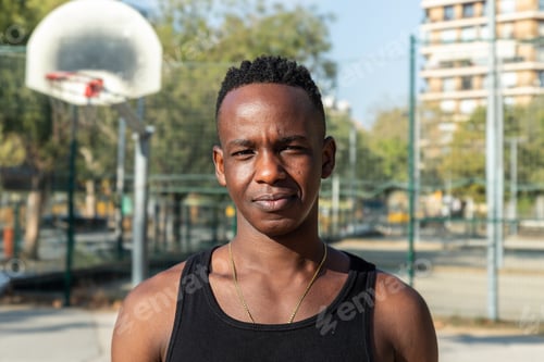 Preview: Headshot portrait of black young man in basketball court outdoors looking at camera.