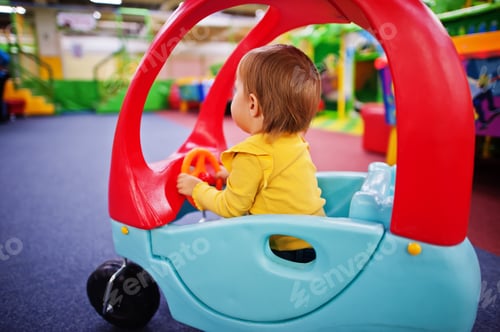 Preview: Cute baby girl rides on a plastic car in indoor play center.