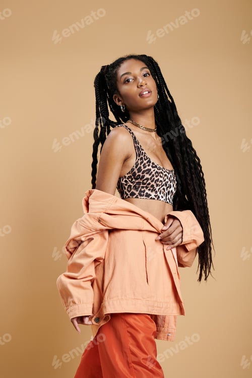 Preview: Stylish young woman exuding confidence in vibrant attire against a warm backdrop