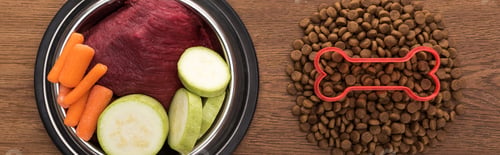 Preview: top view of dry pet food with bone near raw vegetables and meat in bowl on wooden table, panoramic