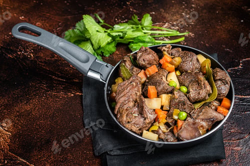 Preview: Irish stew with beef meat, potatoes, carrots and herbs in a skillet. Dark background. Top view