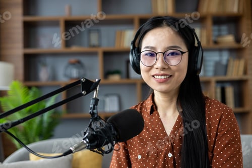 Vista previa: Smiling asian woman with headphones recording a podcast in cozy home studio with microphone and