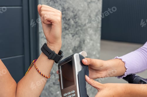 Preview: closeup Customer’s hand paying with smartwatch at card reader held by delivery woman