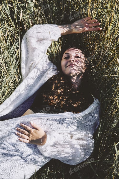 Preview: Young woman resting in sunlit rye field with shadows on face