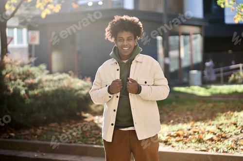 Preview: Happy young gen z African American guy standing at sunny street in city park.