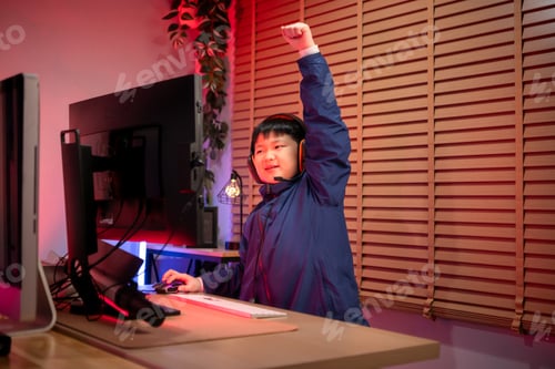 Preview: A boy gamer wearing headphones and playing on a desktop computer in a colorful gaming setup