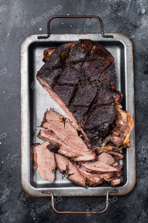 Preview: Roast Venison leg, baked meat of roe deer with bone on a tray with herbs. black background. top view