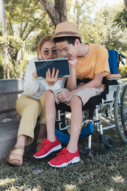 Preview: Special need child on wheelchair using technology with his parent on nature background
