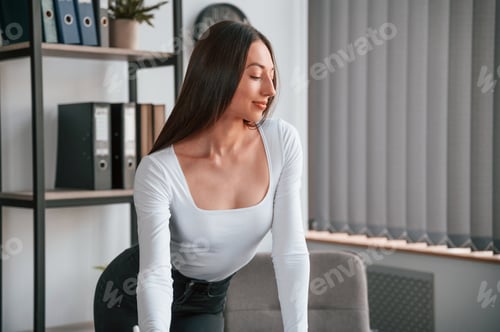 Preview: Standing by the table. Young beautiful woman in white clothes is in the office